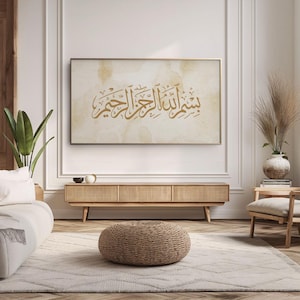May include: A beige living room with a brown wooden media console and a brown woven ottoman. A framed print with gold Arabic calligraphy hangs on the wall above the console.