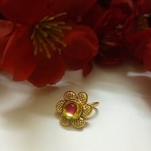 Peut inclure: Un anneau de nez en forme de fleur de couleur dorée avec une pierre précieuse rouge au centre.