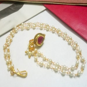 May include: A gold nose ring with a pink gem and a double strand of white pearls.