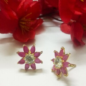 Puede incluir: Un par de pendientes de oro en forma de flor con piedras preciosas rosas y una piedra central transparente.