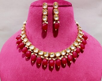 May include: A gold necklace with a red and white stone design. The necklace has a matching pair of earrings with red and white stones.