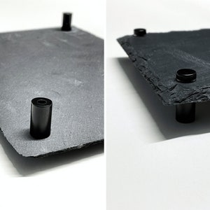 Puede incluir: Una bandeja de servir de pizarra negra con cuatro patas de metal negro. La bandeja es rectangular y tiene una superficie rugosa y natural.