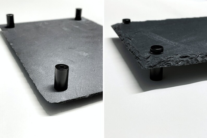 Puede incluir: Una bandeja de servir de pizarra negra con cuatro patas de metal negro. La bandeja es rectangular y tiene una superficie rugosa y natural.
