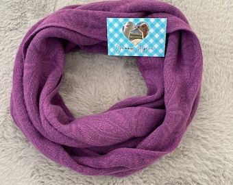 May include: A circular, purple infinity scarf made of a soft, textured material. A small tag with a heart-shaped cutout and the text "Yannys Alpaca" is attached. The scarf is displayed on a gray, fluffy surface.