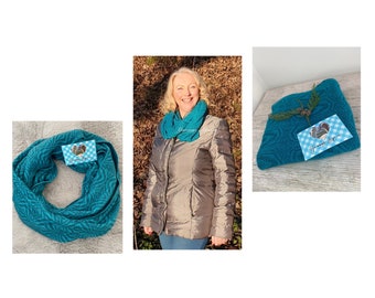 May include: Teal-colored infinity scarf with a geometric pattern. The scarf is displayed in three different ways: worn, folded, and rolled. A tag with a logo is attached to each scarf. The woman in the image is wearing a silver puffer jacket.