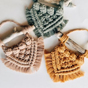 Peut inclure: Trois tentures murales en macramé aux couleurs douces : vert sauge, beige et jaune moutarde. Chaque pièce est fixée à un morceau de bois flotté et présente un motif noué avec des franges. Ces pièces faites à la main sont parfaites pour ajouter une touche bohème.