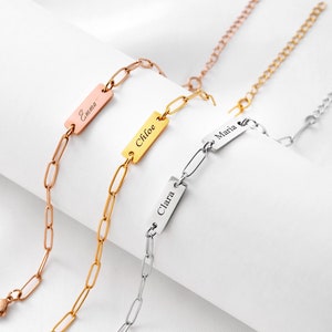 May include: Three personalised chain bracelets in rose gold, gold, and silver. Each bracelet features a rectangular nameplate engraved with a name: "Emma", "Chloe", and "Clara". The bracelets have a delicate, elongated link chain.