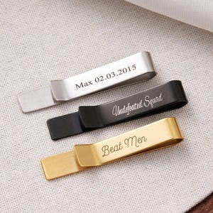 May include: Three rectangular metal tie clips in silver, black, and gold tones. The silver clip is engraved with "Max 02.03.2015", the black clip features the script text "Undefeated Squad", and the gold clip is engraved with the script text "Beat Men".