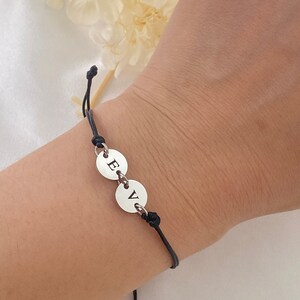 May include: A black cord bracelet with three silver charms, each with a letter, spelling out "E V"