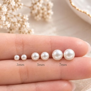 May include: Three pairs of round white pearl stud earrings arranged by size. The pairs are labeled with text indicating diameters of 3mm, 5mm, and 7mm. Each pair consists of two identical spherical white pearls with a smooth, lustrous finish.