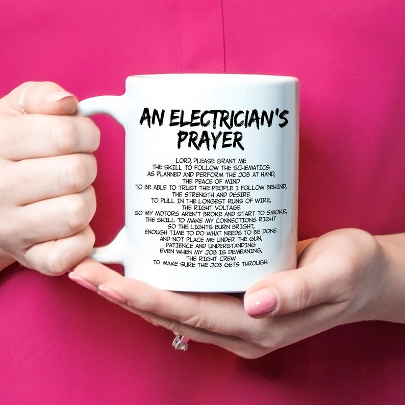 May include: White ceramic mug with the text "AN ELECTRICIAN'S PRAYER" in black. The prayer is printed in a black, easy-to-read font. The mug is held by a person with pink nail polish.