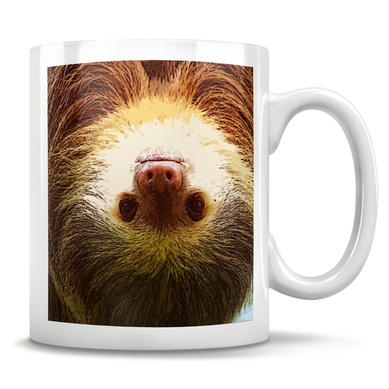 May include: A white ceramic coffee mug with a brown and tan sloth face printed on it. The sloth is upside down and looking directly at the viewer.