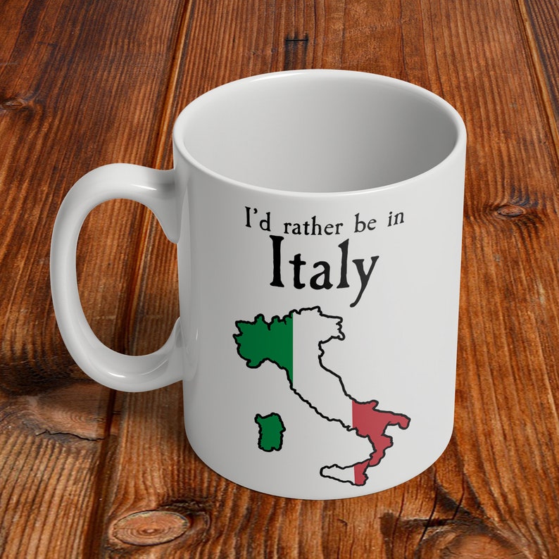 Puede incluir: Taza de cer&aacute;mica blanca con un contorno negro de la pen&iacute;nsula italiana y los colores de la bandera italiana. El texto "Prefiero estar en Italia" est&aacute; impreso en la taza.
