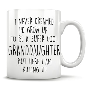May include: White ceramic mug with a curved handle. The mug features black text that reads, "I NEVER DREAMED I'D GROW UP TO BE A SUPER COOL GRANDDAUGHTER BUT HERE I AM KILLING IT!" A gift for a granddaughter.