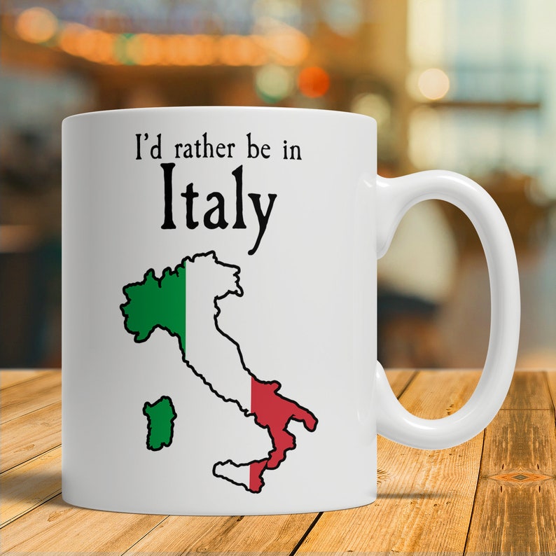 Puede incluir: Taza de cer&aacute;mica blanca con un contorno negro de Italia y los colores de la bandera italiana. El texto "Prefiero estar en Italia" est&aacute; impreso en la taza.