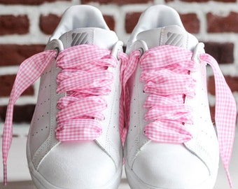 May include: A pair of white leather sneakers with pink gingham ribbon laces. The laces are tied in a bow on the top of the shoes.