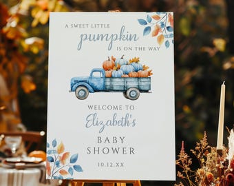Puede incluir: Un letrero blanco sobre un caballete de madera con el texto "A sweet little pumpkin is on the way". Una ilustración de camión azul transporta calabazas. El letrero da la bienvenida a la fiesta de bienvenida de Elizabeth.