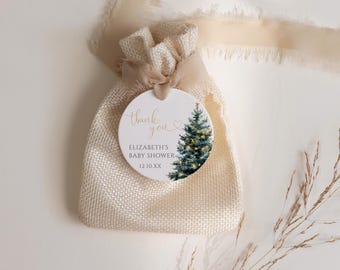 Op de afbeelding: Een kleine, beige jute cadeauzak met een crèmekleurig lint en een rond label. Het label bevat de tekst "thank you" in gouden letters, de naam "Elizabeth's Baby Shower" en een aquarel illustratie van een kerstboom.