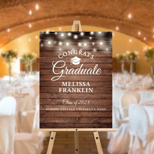 May include: A rustic wooden sign with a white background and string lights. The sign says "Congrats Graduate" with a graduation cap icon, "Melissa Franklin", "Class of 2024", and "School College University Name".