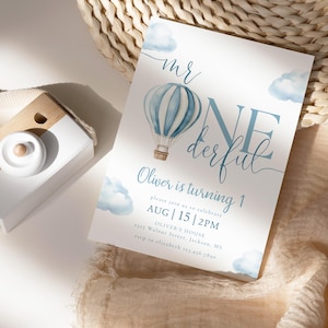 May include: A white invitation card with blue watercolor clouds and a hot air balloon illustration. The text reads "Mr. One-derful" and announces Oliver's first birthday, including the date, time, and location.