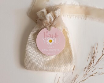 Op de afbeelding: Een kleine, beige jute cadeauzak met een crèmekleurig lint. Een roze ronde tag met de woorden "Thank You" en "Lily's Baby Shower" is bevestigd. De tag heeft een madeliefjesafbeelding en de datum 10.08.XX.