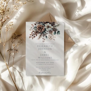 May include: Wedding invitation featuring floral and pinecone illustrations in shades of brown, blue, and white. The invitation includes the names Elizabeth Johnson & James Williams, along with the wedding date and location. The invitation is placed on a white fabric background.