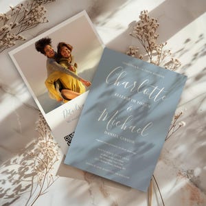 May include: Wedding invitation suite featuring a photo card and a blue invitation card. The invitation card has the names "Charlotte & Michael" in elegant script. The photo card shows two people. Dried flowers and shadows add to the aesthetic.