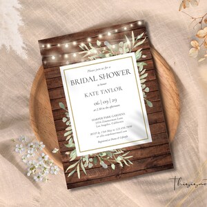 May include: A bridal shower invitation with a rustic wood background. The invitation features the text "BRIDAL SHOWER" and details for Kate Taylor's shower. It is decorated with watercolor greenery and string lights. The invitation is on a wooden tray.