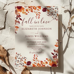 Puede incluir: Una invitación de boda con un fondo crema y un borde floral con temática otoñal. El texto "fall in love" está en una fuente cursiva, con los nombres Elizabeth Johnson y James Williams debajo. La fecha es el 21 de octubre de 20XX.