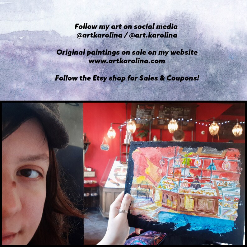 May include: A woman holds up a watercolor painting of a bakery interior. The painting is on a dark background and the woman is wearing a black hat and a colorful scarf. The painting depicts a bakery counter with pastries and a red wall behind it. The text on the painting reads "My Donuts".