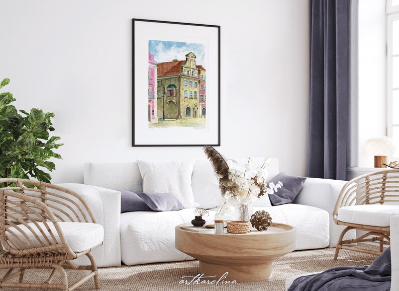 May include: A watercolor painting of a building with a pink facade and a yellow facade. The building has a large window and a balcony. The painting is framed in a black frame and is hanging on a white wall.