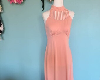 May include: A peach-colored maxi dress with a halter neckline and a cutout detail at the neckline. The dress has a fitted bodice and a flowing skirt.