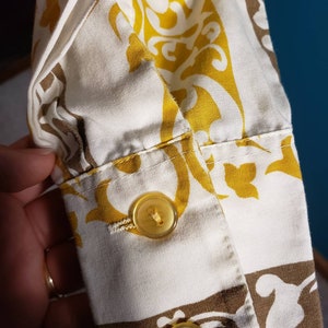 May include: Close-up of a white and yellow patterned fabric with two yellow buttons. The fabric has a brown and white pattern in the lower right corner.