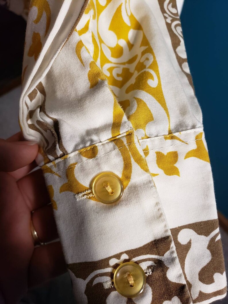 May include: Close-up of a white and yellow patterned fabric with two yellow buttons. The fabric has a brown and white pattern in the lower right corner.