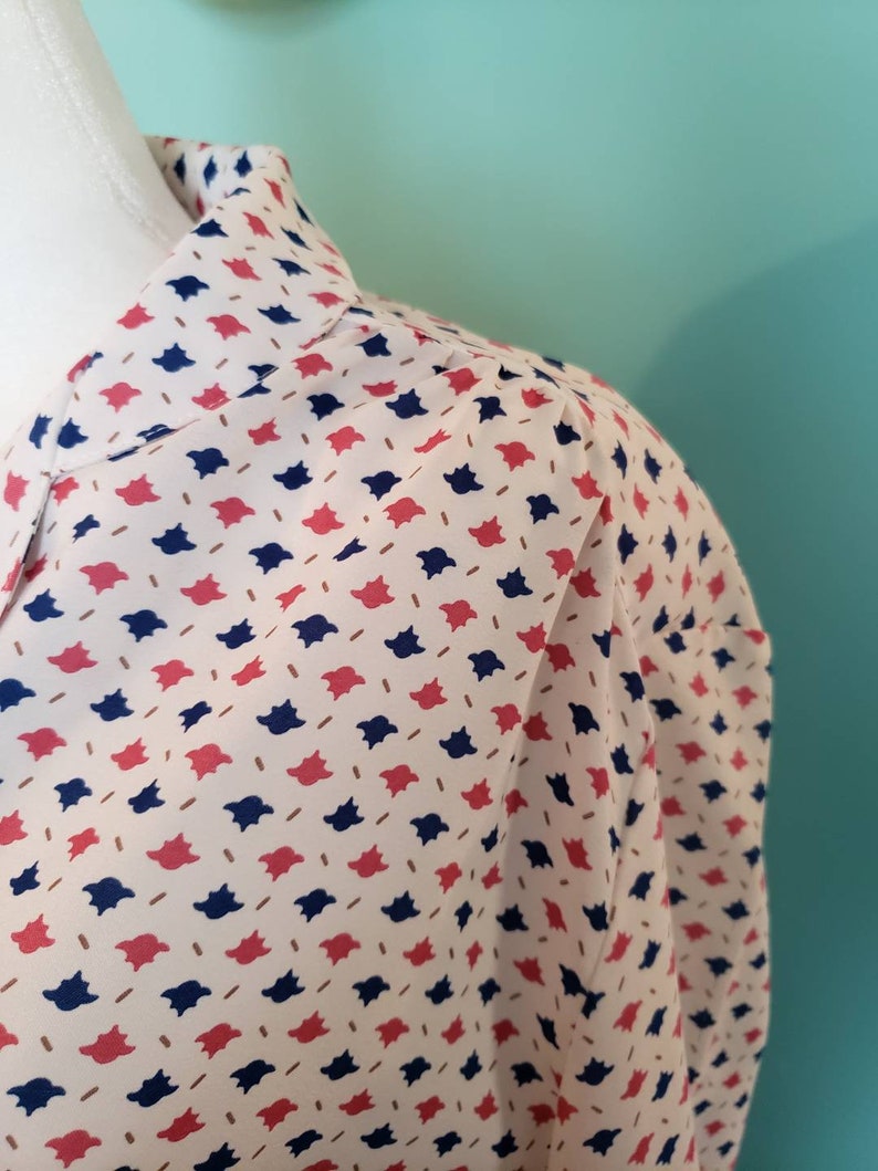 May include: A white blouse with a collar and a pattern of red and blue geometric shapes.