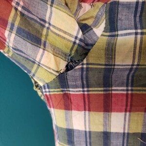 May include: A close-up of a red, blue, yellow, and white plaid fabric with a tear in the fabric.