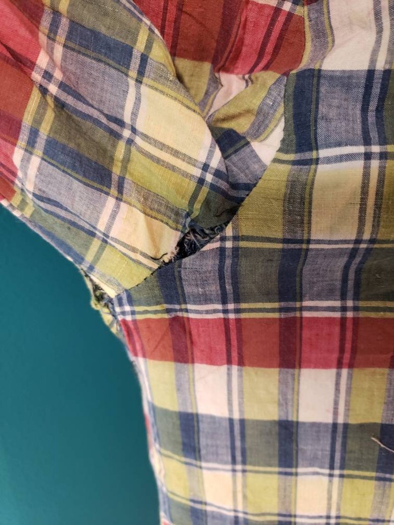 May include: A close-up of a red, blue, yellow, and white plaid fabric with a tear in the fabric.