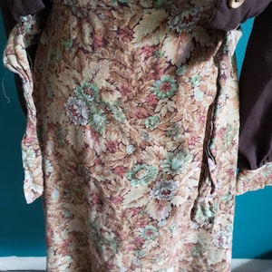 K&ouml;nnte beinhalten: Ein brauner Wickelrock mit einem Blumendruck mit gr&uuml;nen, rosa und wei&szlig;en Blumen. Der Rock hat einen G&uuml;rtel zum Binden in der Taille.