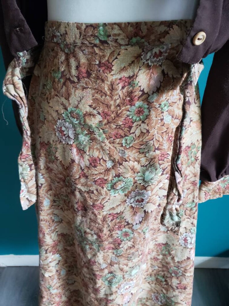 K&ouml;nnte beinhalten: Ein brauner Wickelrock mit einem Blumendruck mit gr&uuml;nen, rosa und wei&szlig;en Blumen. Der Rock hat einen G&uuml;rtel zum Binden in der Taille.