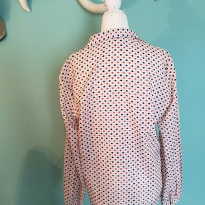 May include: A white long-sleeved blouse with a geometric pattern of red, blue, and white diamonds.