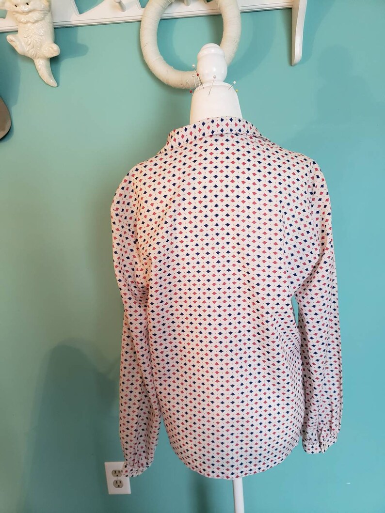 May include: A white long-sleeved blouse with a geometric pattern of red, blue, and white diamonds.