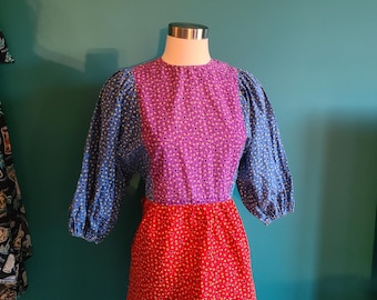 May include: A vintage dress with a patchwork design. The dress has a blue, purple, and red floral print. The dress has a round neckline and 3/4 sleeves.