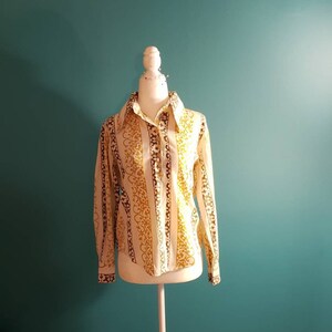 May include: A white long-sleeved button-up shirt with brown and gold vertical stripes and a floral pattern.