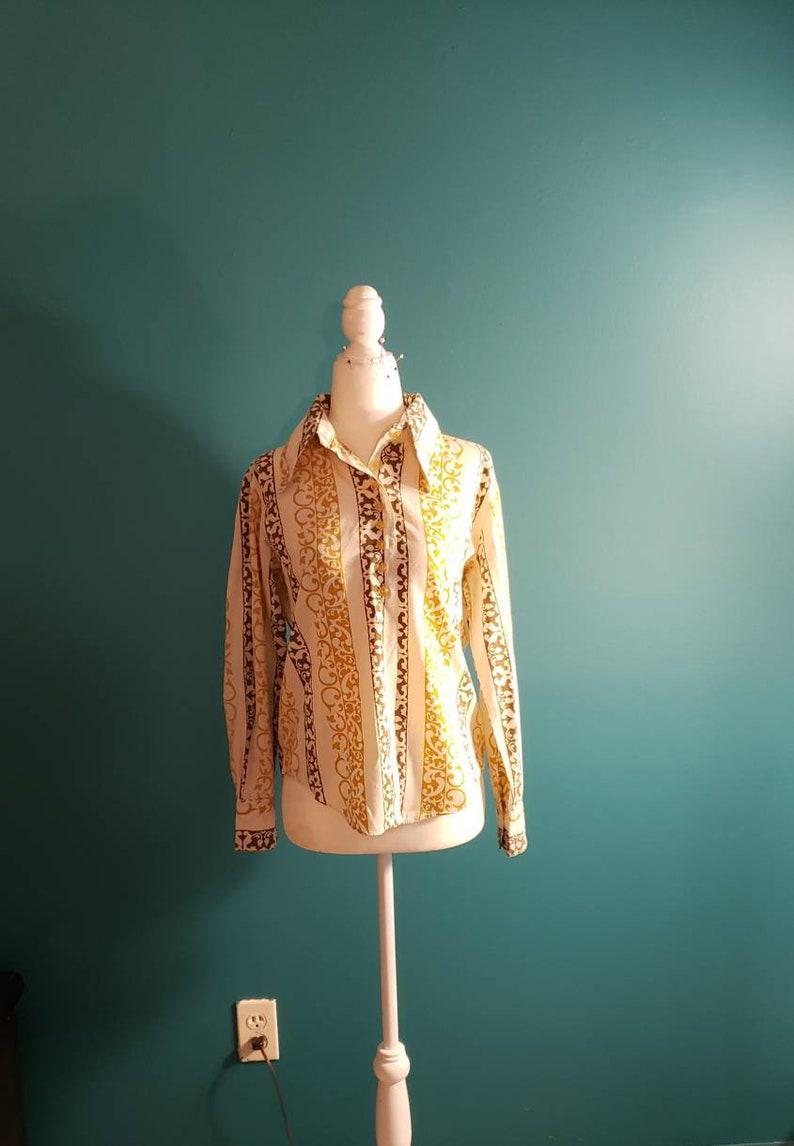 May include: A white long-sleeved button-up shirt with brown and gold vertical stripes and a floral pattern.