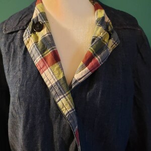 May include: A dark blue denim jacket with a plaid lining. The lining is visible at the collar and is a mix of red, green, blue, and white.