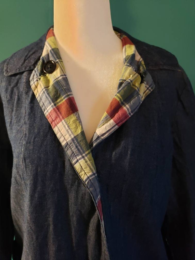 May include: A dark blue denim jacket with a plaid lining. The lining is visible at the collar and is a mix of red, green, blue, and white.