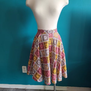 May include: A brown, pink, and yellow patterned skirt with a flared silhouette. The skirt is made of a woven fabric and has a geometric design.