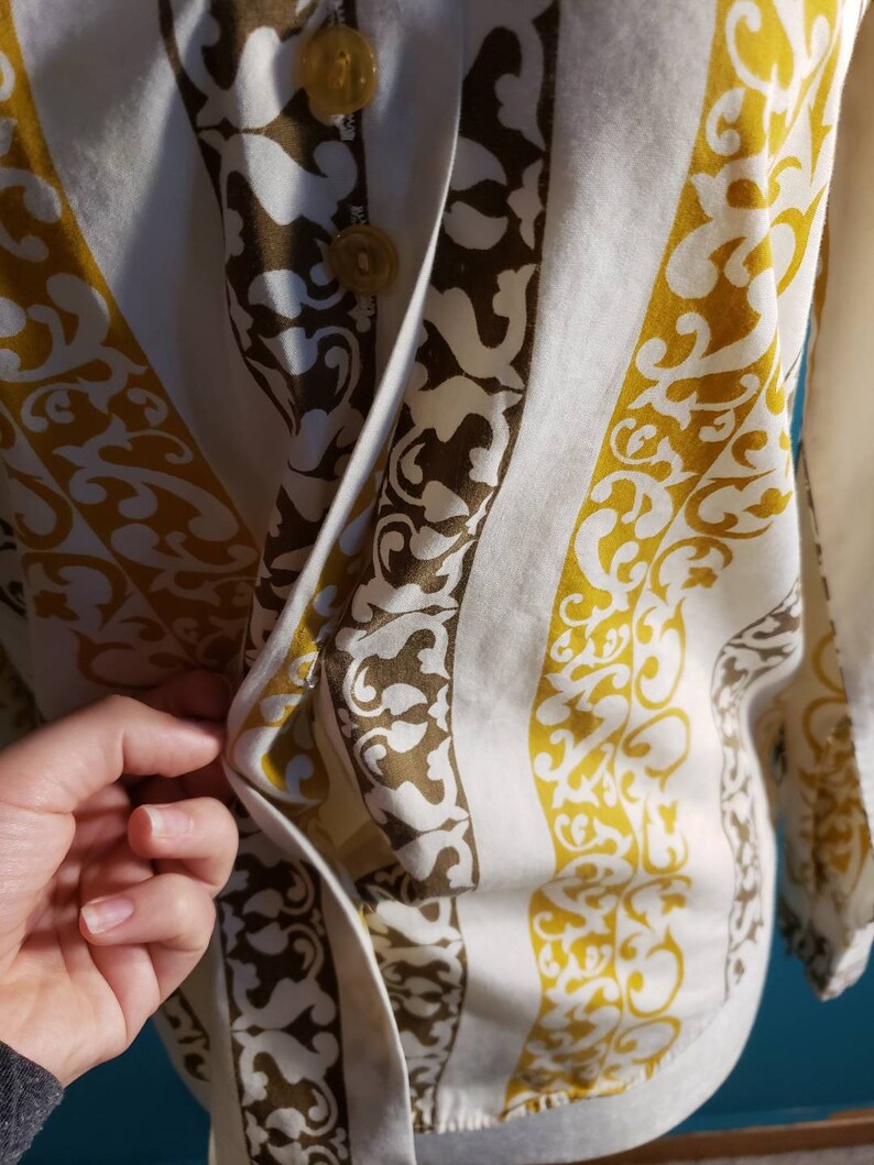May include: A white button-up shirt with a vertical striped pattern. The stripes are a dark brown and a mustard yellow. The shirt has a button closure and a collar.