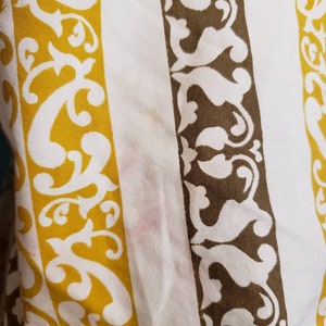 May include: White fabric with brown and yellow stripes. The stripes have a white floral pattern.