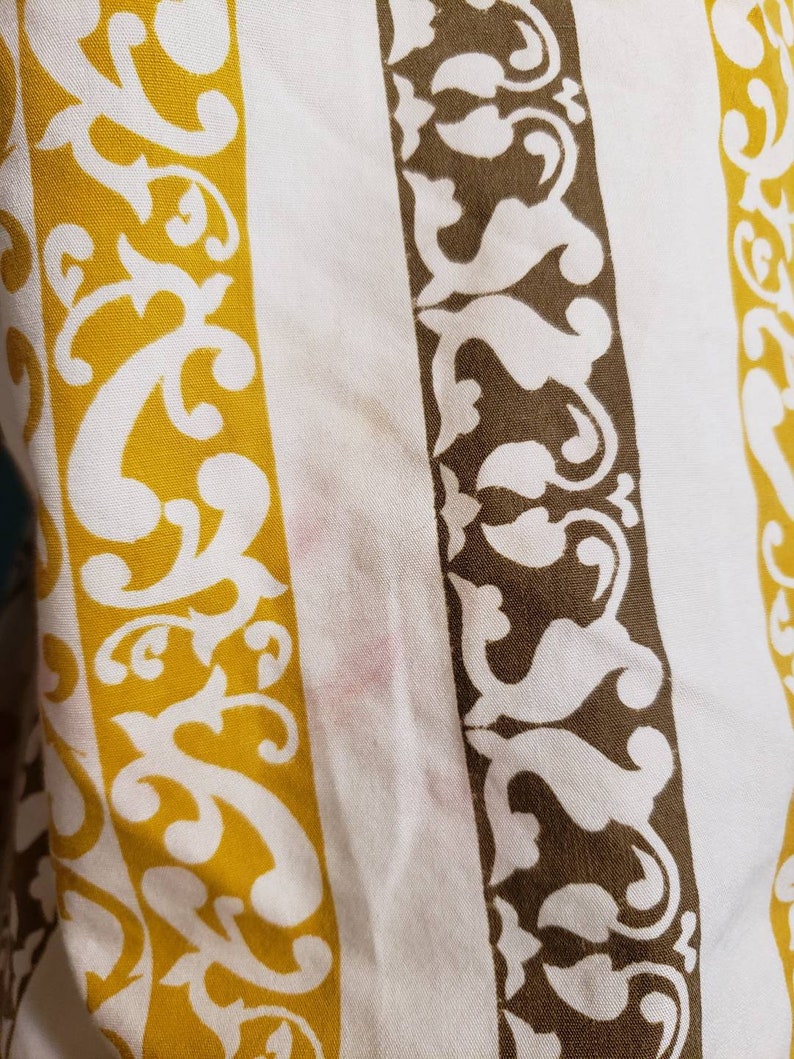 May include: White fabric with brown and yellow stripes. The stripes have a white floral pattern.